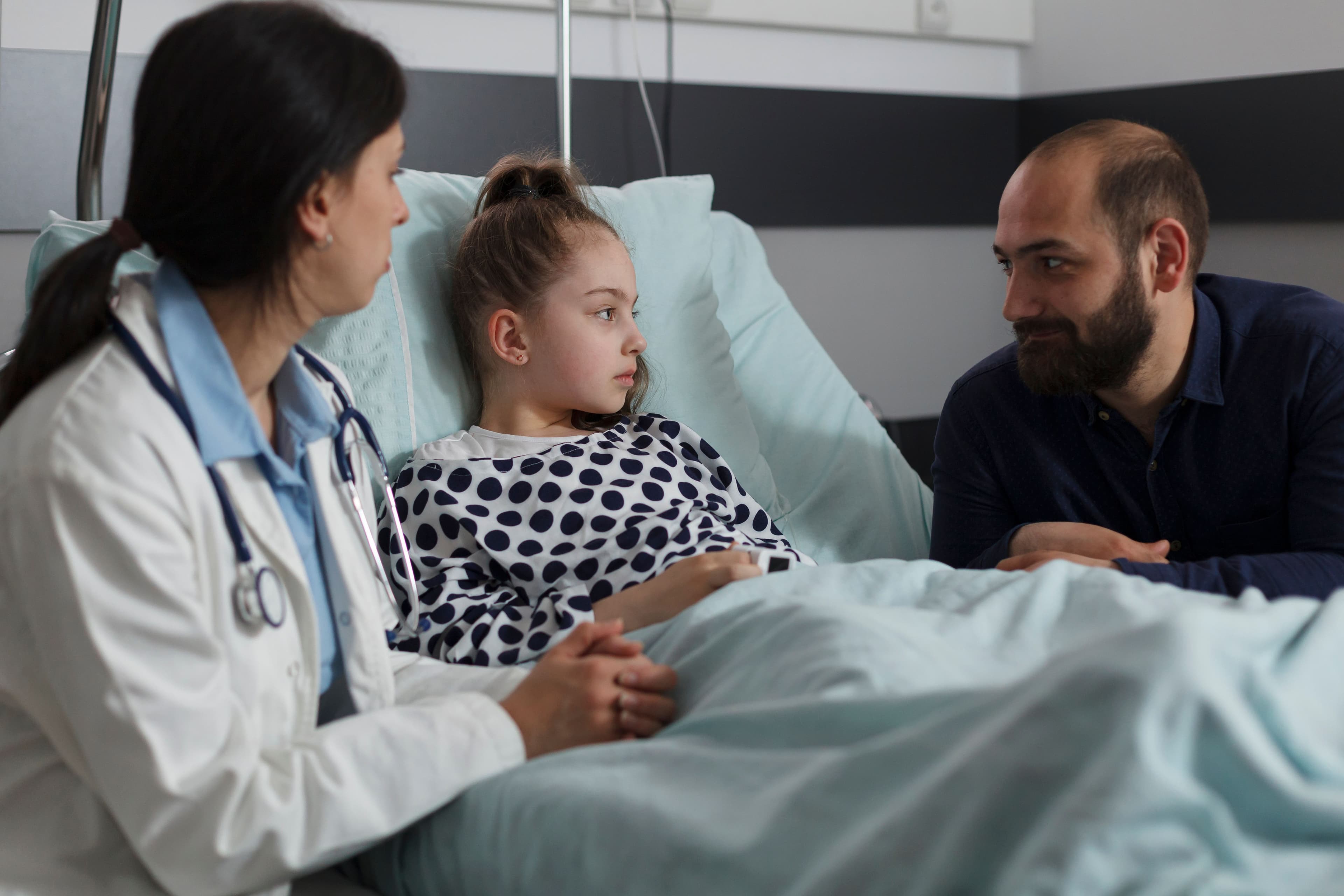 photologuephotos2022-10pediatrician-examining-ill-kid-health-condition-while-discussing-with-parent-caring-father-sitting-next-to-sick-daughter-resting-in-hospital-pediatric-ward-while-doctor-presenting-treatment-schemejpg