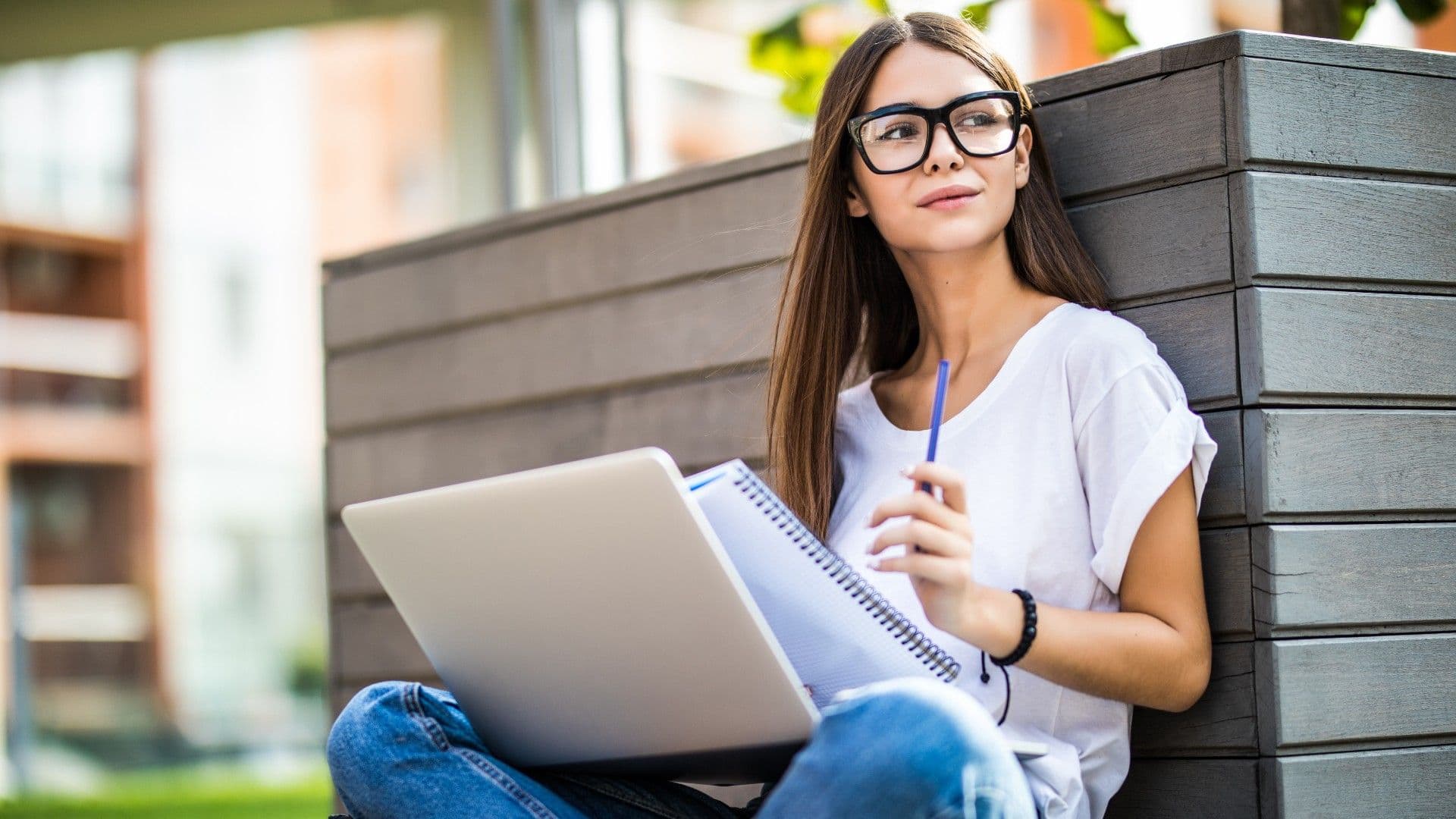 photologuephotos2023-03mujer-joven-feliz-ropa-casual-gafas-usando-computadora-portatil-moderna-tomando-notas-mientras-sentado-banco-calle-ciudadjpg
